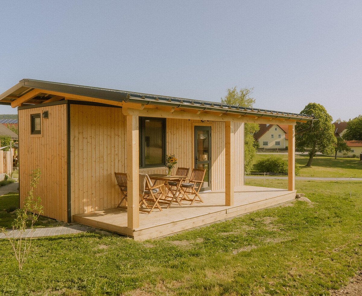 Ein gemütliches Holzhaus des Bauernhofs mit einer überdachten Terrasse und einer einladenden Sitzgruppe im Grünen.