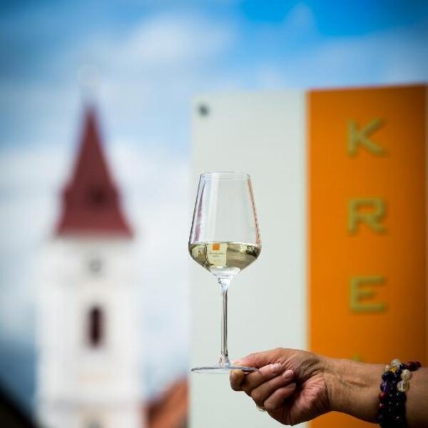 Ein Glas Weißwein vor der Kulisse eines Kirchturms, passend zur regionalen Umgebung des Hofes.