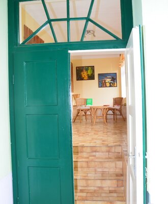 Die offene grüne Tür des Hofes führt in die Veranda mit Fliesenboden, Holztisch und Korbstühlen.