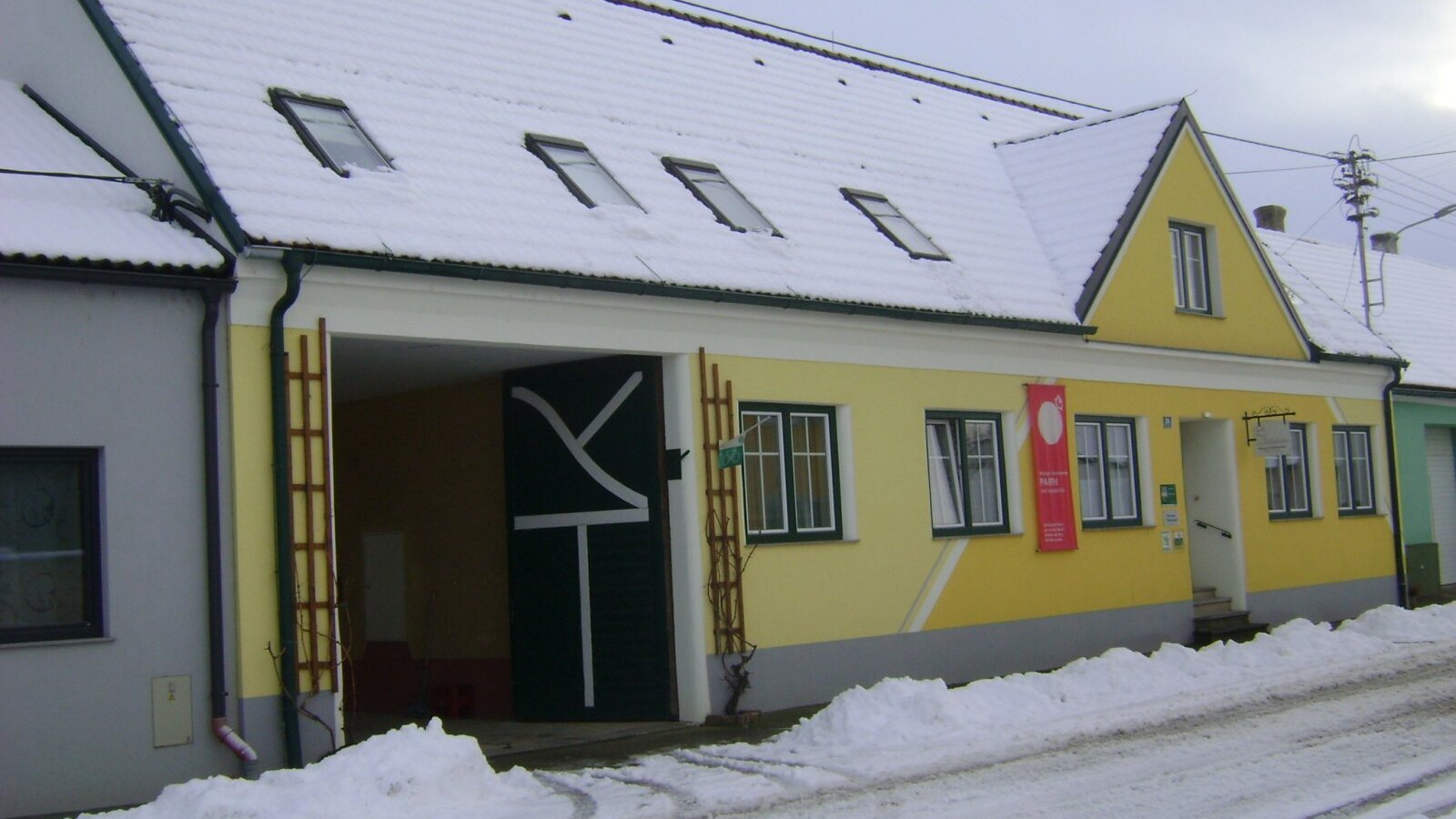 Die Außenansicht des Hofs mit gelber Fassade, schneebedecktem Dach und Dachfenstern im Winter.