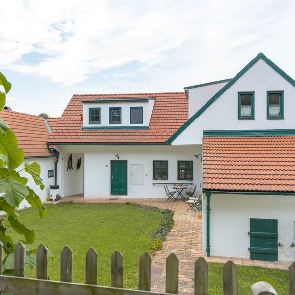 Der Winzerhof von außen mit weißer Fassade, gr&uuml;nen Fensterl&auml;den und einer Terrasse mit Sitzgelegenheiten im Rasen.