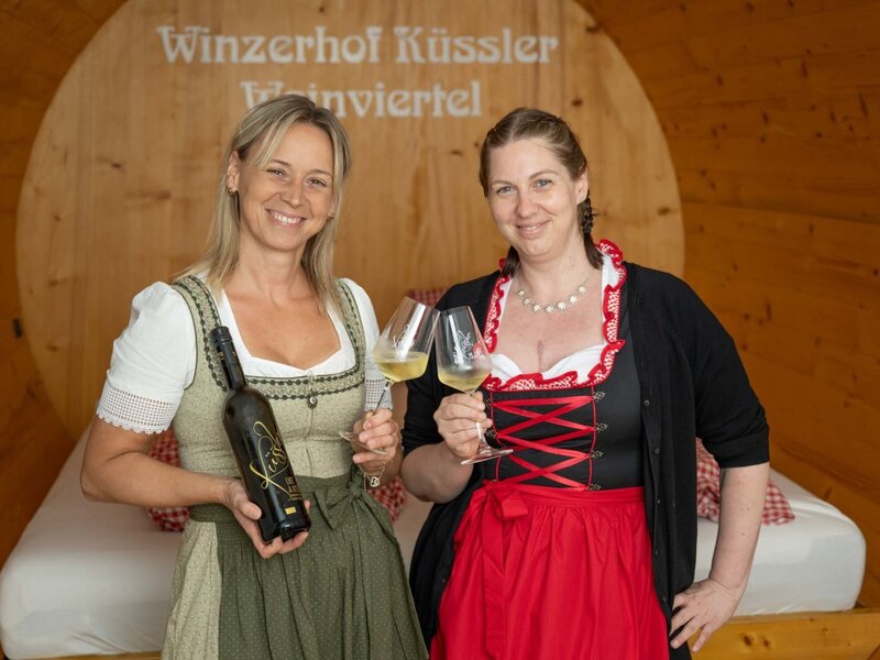 Zwei Mitarbeiter des Winzerhofs Küssler präsentieren Wein in einer der Weinfass-Suiten.