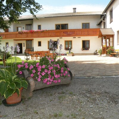 Außenansicht des Bauernhofs mit Gartenbereich, Sitzgelegenheiten und blumengeschmücktem Balkon.