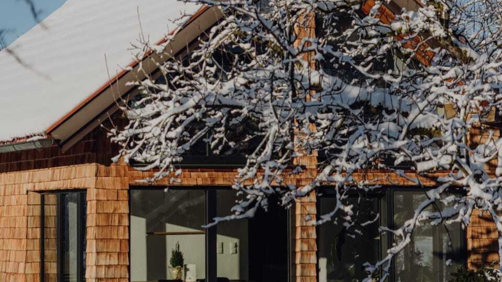 Das Chalet im Obstgarten des Bauernhofs, mit Holzschindelfassade und großen Fenstern, umgeben von Schnee und Bäumen.