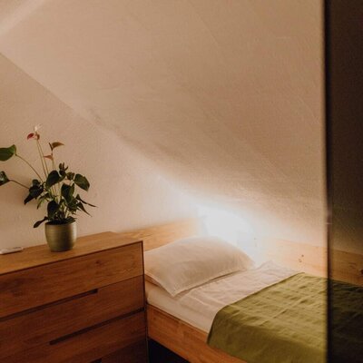 Einzelbett im Bauernhof mit Holzrahmen, grüner Tagesdecke, Dachschräge und Holzkommode.