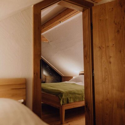 Blick in ein Schlafzimmer des Bauernhofs mit Holzbett, grüner Decke und Dachschräge.