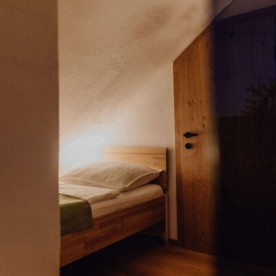 Einzelbett im Bauernhof mit Holzbettrahmen, Holzboden und Dachschräge.