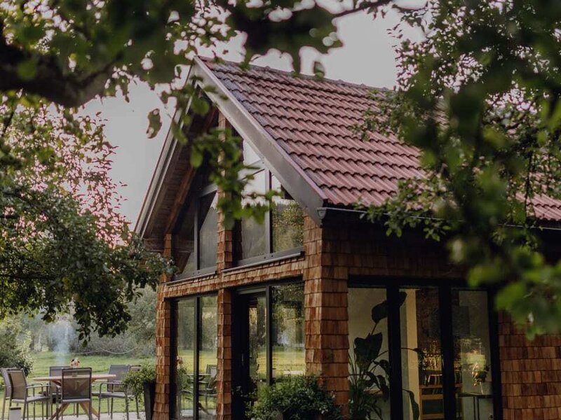Das gemütliche Chalet im Obstgarten des Bauernhofs mit einer gepflasterten Terrasse und großen Fensterfronten.
