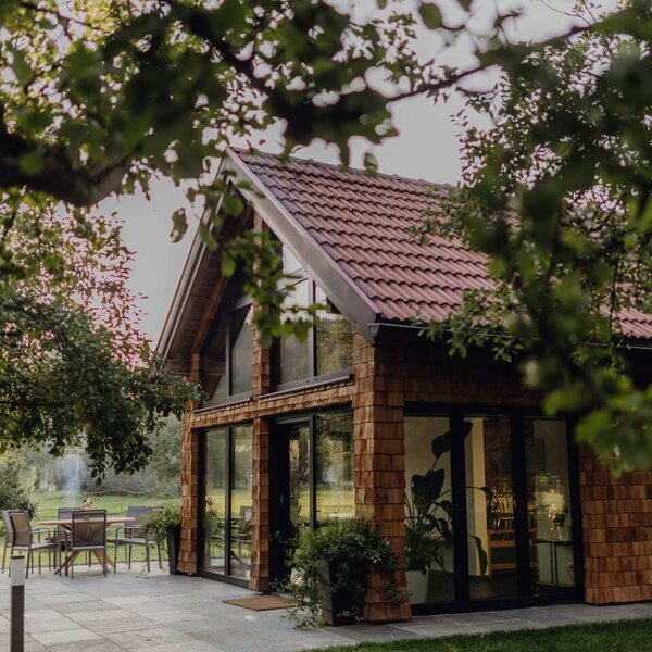 Das gemütliche Chalet im Obstgarten des Bauernhofs mit einer gepflasterten Terrasse und großen Fensterfronten.