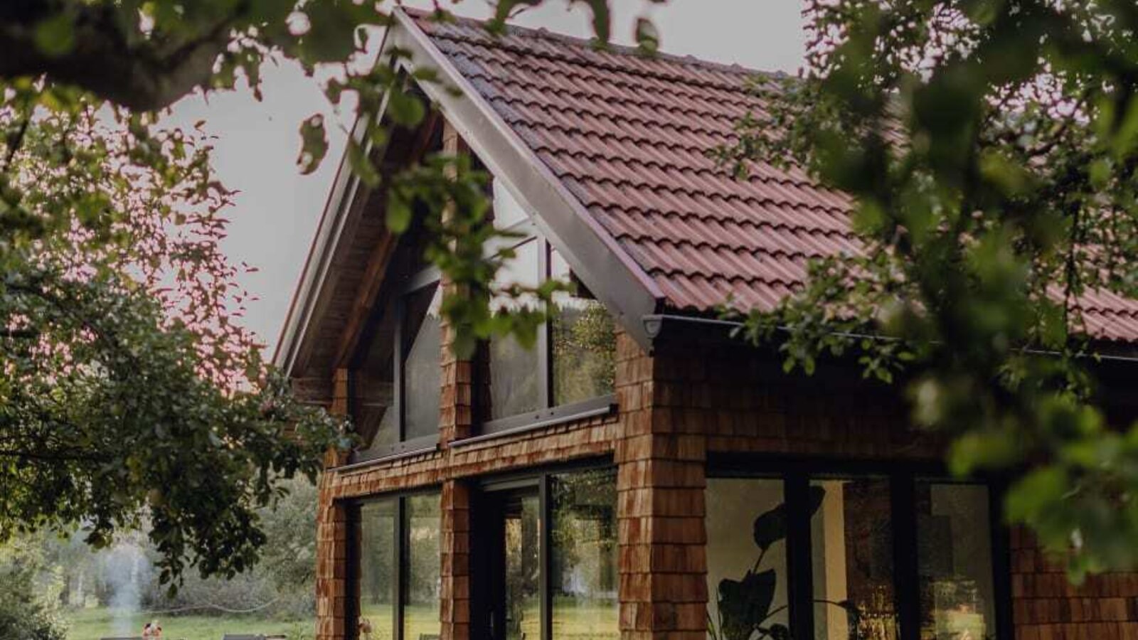 Das gemütliche Chalet im Obstgarten des Bauernhofs mit einer gepflasterten Terrasse und großen Fensterfronten.