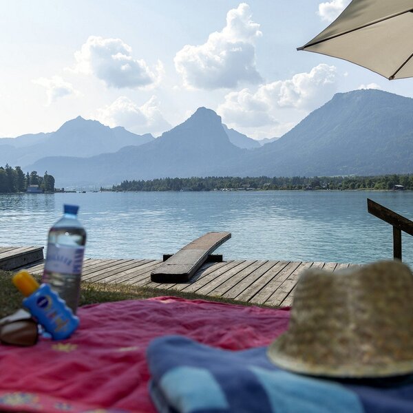 Privater Seezugang des Bauernhofs mit Holzsteg, Sonnenschirm und Panoramablick auf den Wolfgangsee und die umliegenden Berge.