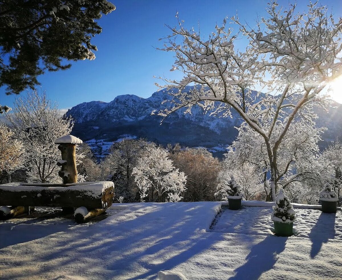 Verschneite Winterlandschaft des Bauernhofs mit Blick auf die Berge und einen Holzbrunnen.