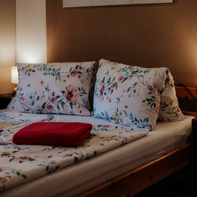 Doppelbett mit floraler Bettwäsche, roten Decken und zwei Nachttischlampen im Bauernhof.