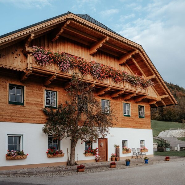 Der Bauernhof mit traditioneller Holzfassade, weißen Wänden und blumengeschmückten Balkonen.