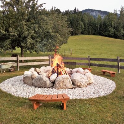 Die Lagerfeuerstelle auf dem Bauernhof mit Sitzbänken und grüner Landschaft.