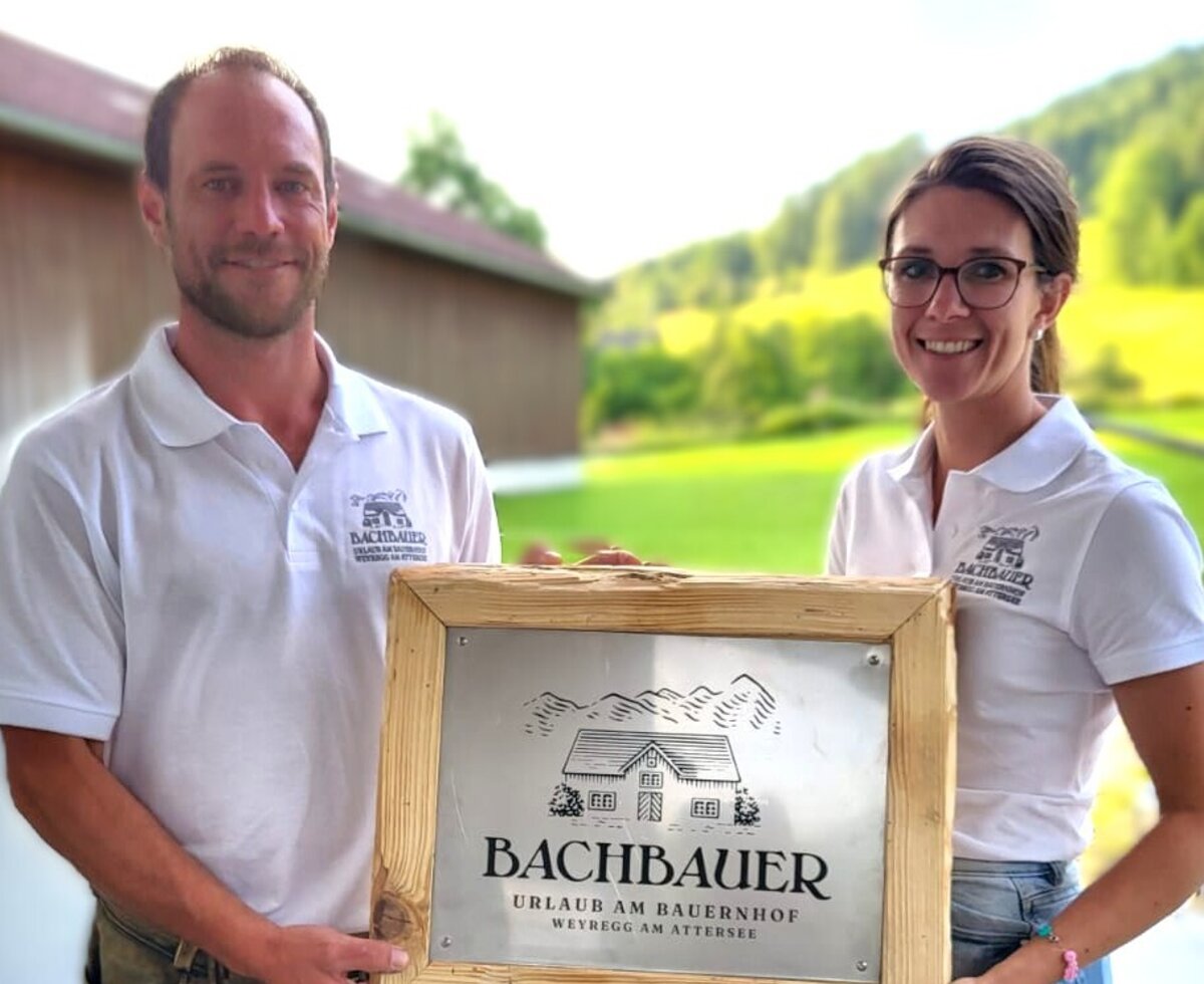 Die Gastgeber des Bauernhofs Bachbauer präsentieren die Namenstafel des Hofes.