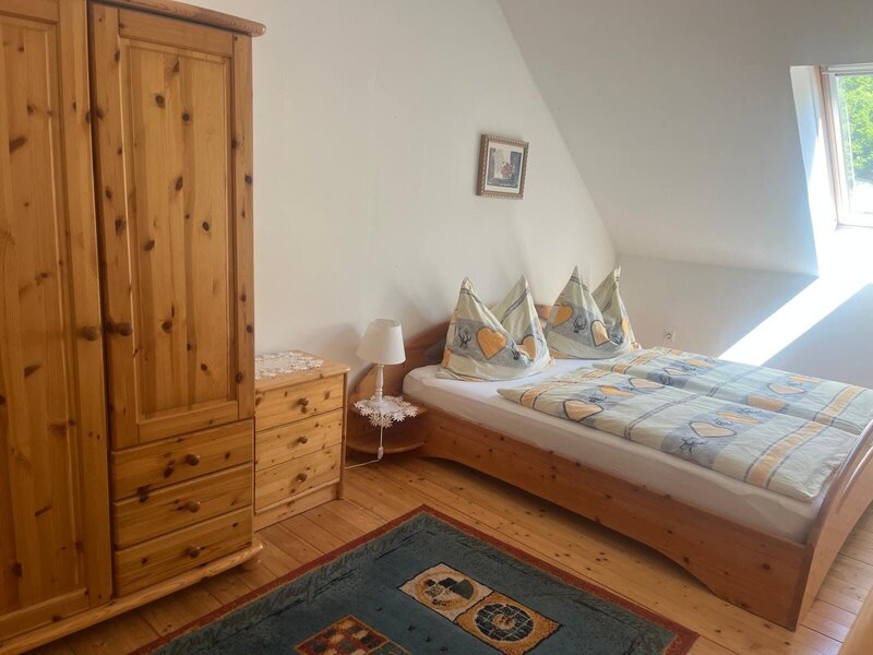 Schlafzimmer im Bauernhof mit Doppelbett, Holzschrank und Fenster.