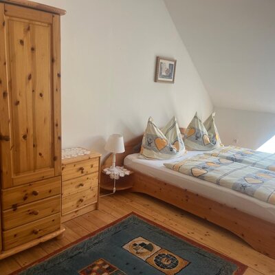 Schlafzimmer im Bauernhof mit Doppelbett, Holzschrank und Fenster.