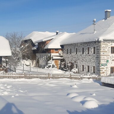 Die schneebedeckten Gebäude des Bauernhofs mit charakteristischer Steinfassade an einem sonnigen Wintertag.