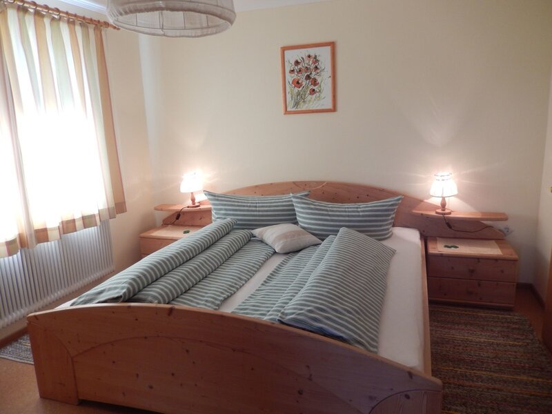 Doppelzimmer im Bauernhof mit Holzbett, zwei Nachttischen mit Lampen und Fenster.