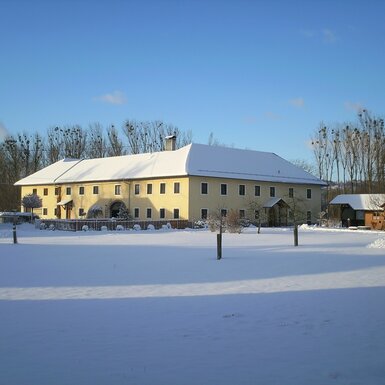 Das Hauptgebäude des Bauernhofs mit schneebedecktem Dach in einer verschneiten Winterlandschaft.