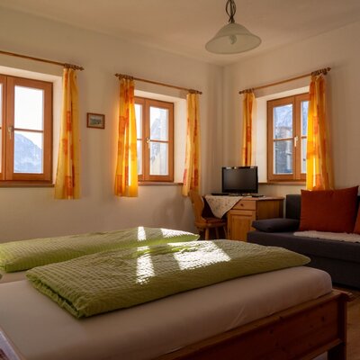 Schlafzimmer im Bauernhof mit zwei Einzelbetten, einem Schlafsofa, einem Schreibtisch mit TV und Fenstern mit Bergblick.