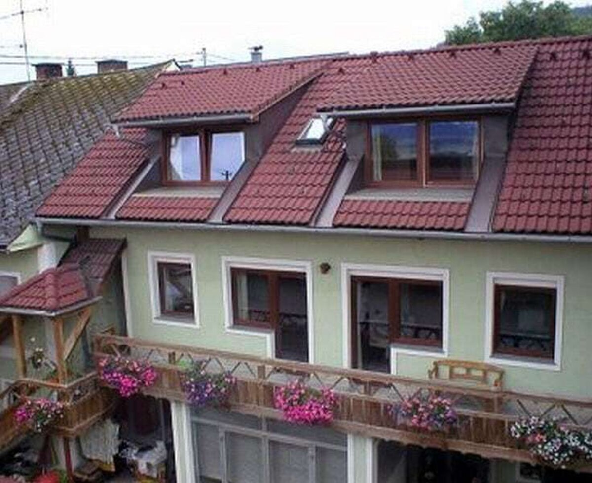 Die hellgrüne Außenfassade des Bauernhofs mit roten Dachziegeln, Dachgauben und Balkonen mit Blumenkästen.