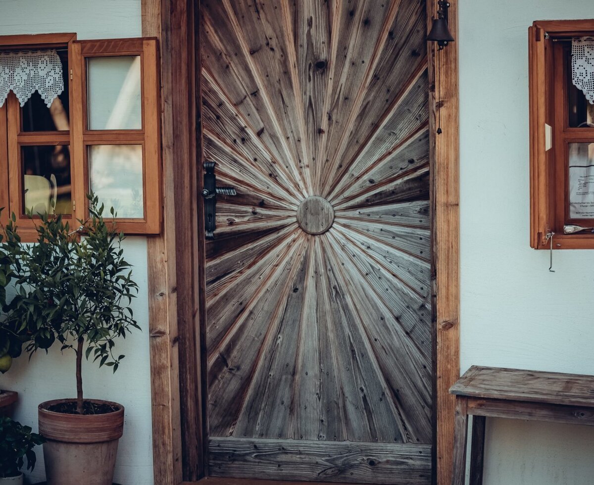 Der Eingang des Bauernhofs mit einer Holztür im Sonnenstrahl-Design, Holzfenstern und Zitronenbäumen in Töpfen.