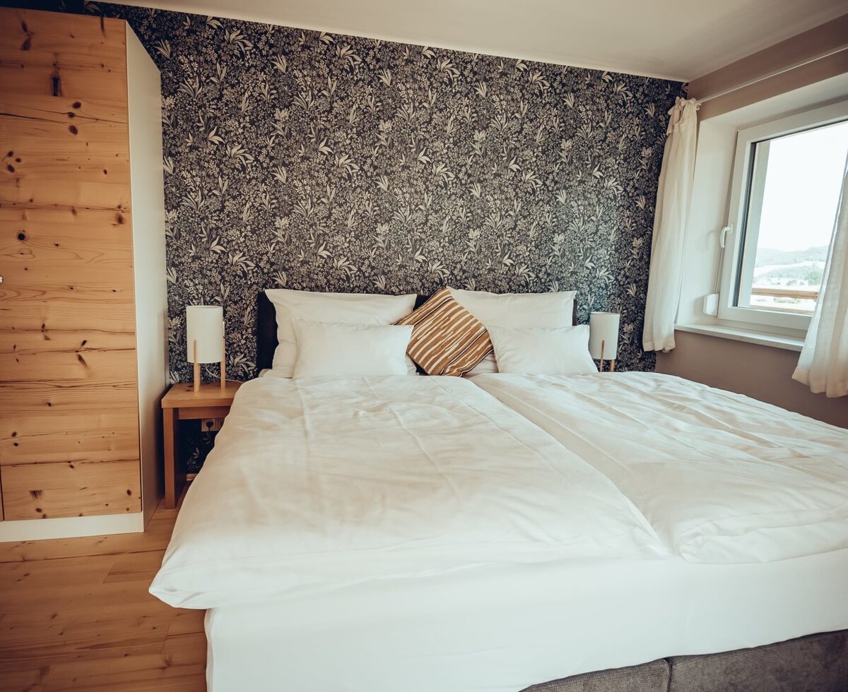 Doppelzimmer im Bauernhof mit Doppelbett, Nachttischen, Lampen, Holzkleiderschrank und Fenster.