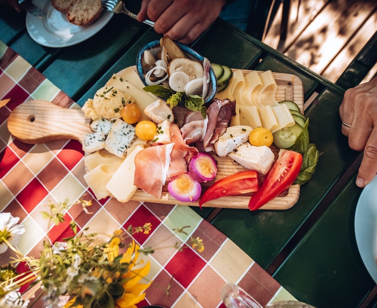 Eine Brotzeitplatte mit verschiedenen Käsesorten, Aufschnitt und frischem Gemüse auf dem Bauernhof.