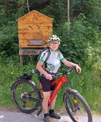 Radfahrer mit E-Bike vor einem Wegweiser zu den Trattenbacher Genussstubn in der Umgebung des Bauernhofs.