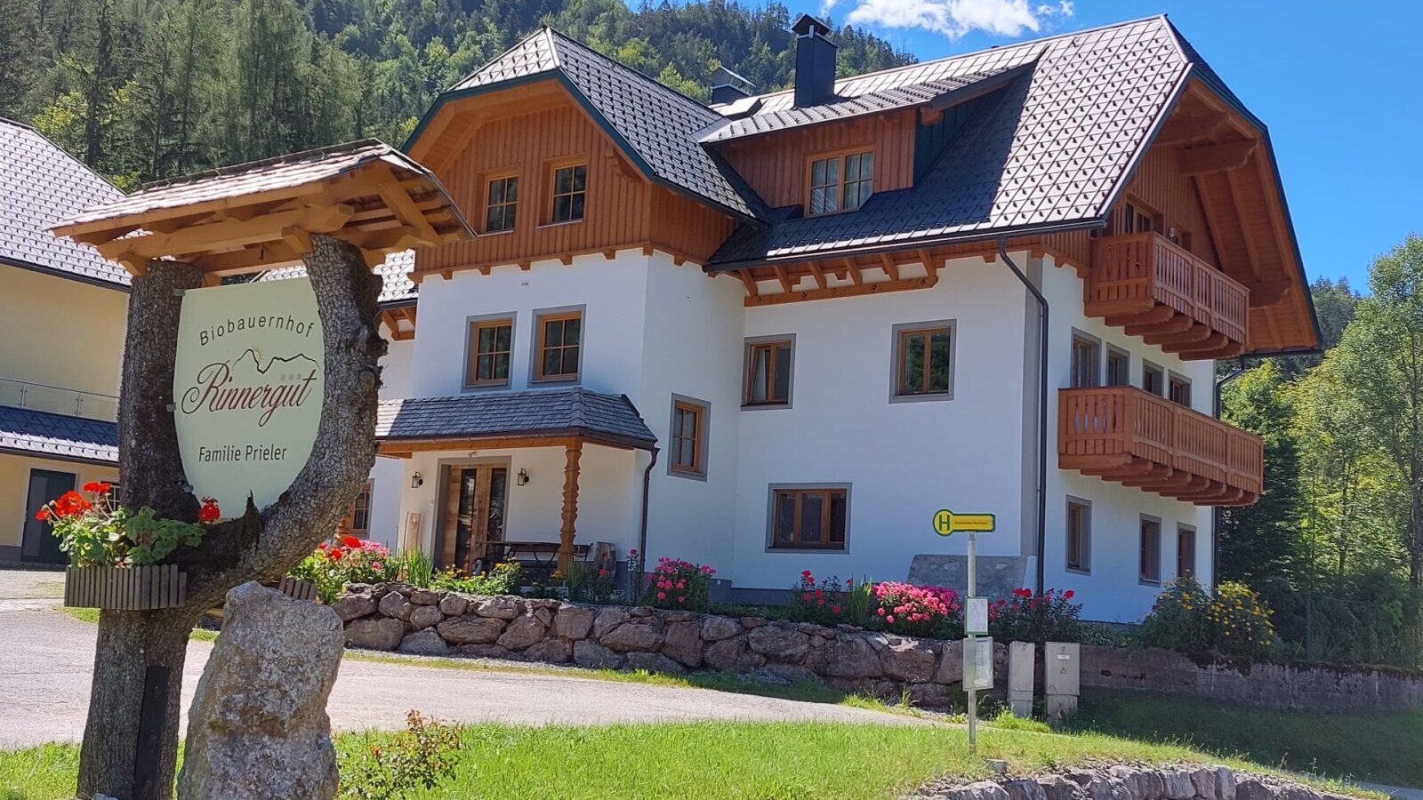 Außenansicht des Bauernhofs Rinnergut mit Holzbalkonen und dem Schild 'Biobauernhof Rinnergut Familie Prieler'.