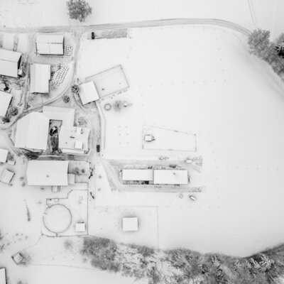 Luftaufnahme des schneebedeckten Bauernhofs mit seinen Gebäuden und umliegenden Feldern.