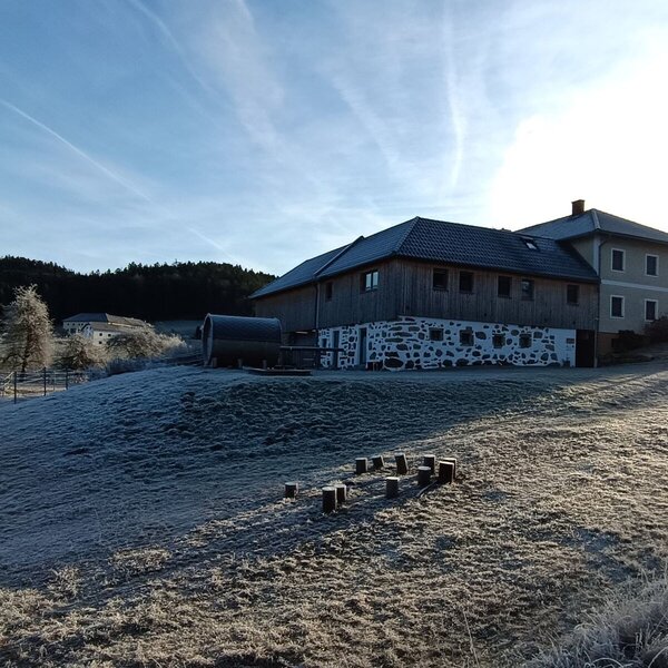Der Bauernhof in einer frostbedeckten Landschaft mit einem Außensaunafass.