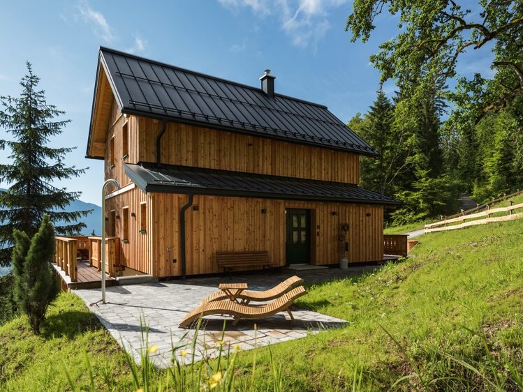 Der Hof mit Holzfassade und schwarzem Dach bietet eine Terrasse mit Sonnenliegen, umgeben von Wald und Wiesen.