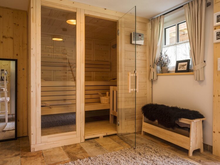 Die Holzsauna im Hof mit Glastür und Holzbänken.