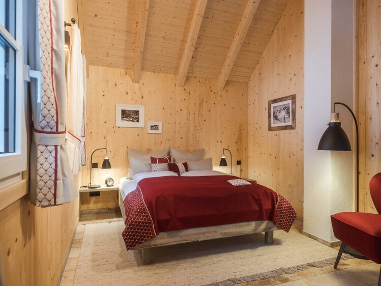 Doppelzimmer im Hof mit Holzwänden, Holzbalkendecke, einem Doppelbett und Sessel.