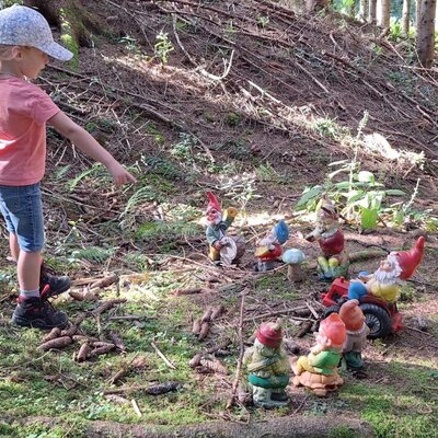Ein Kind zeigt auf eine Gruppe von Gartenzwergen in der Waldumgebung des Bauernhofs.