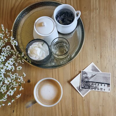 Ein einladendes Arrangement im Appartement mit einer frischen Tasse Kaffee, zarten weißen Blumen und einem dekorativen Tablett auf einem Holztisch.