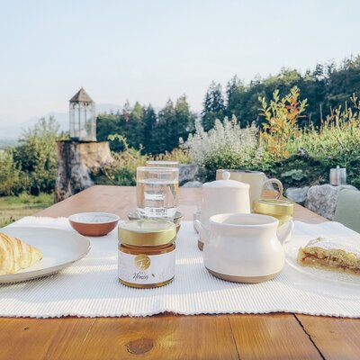 Ein einladender Frühstückstisch im Freien mit frischem Gebäck und regionalem Bio-Honig vor der malerischen Naturkulisse des Bauernhofs.