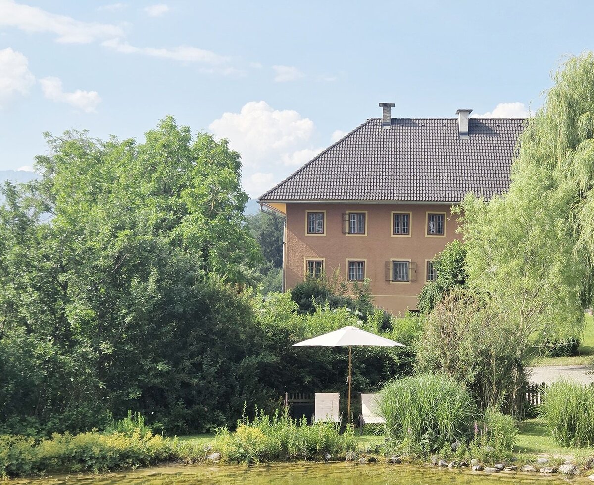 Die idyllische Außenansicht des Bio-Bauernhofs mit den Ferienapartments, umgeben von einem naturnahen Biotop und gemütlichen Liegestühlen im Grünen.