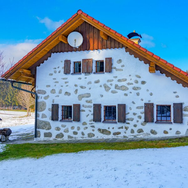 Außenansicht des Bauernhofs mit Fassade aus Stein und weißem Putz, Holzläden und verschneitem Gartenbereich.