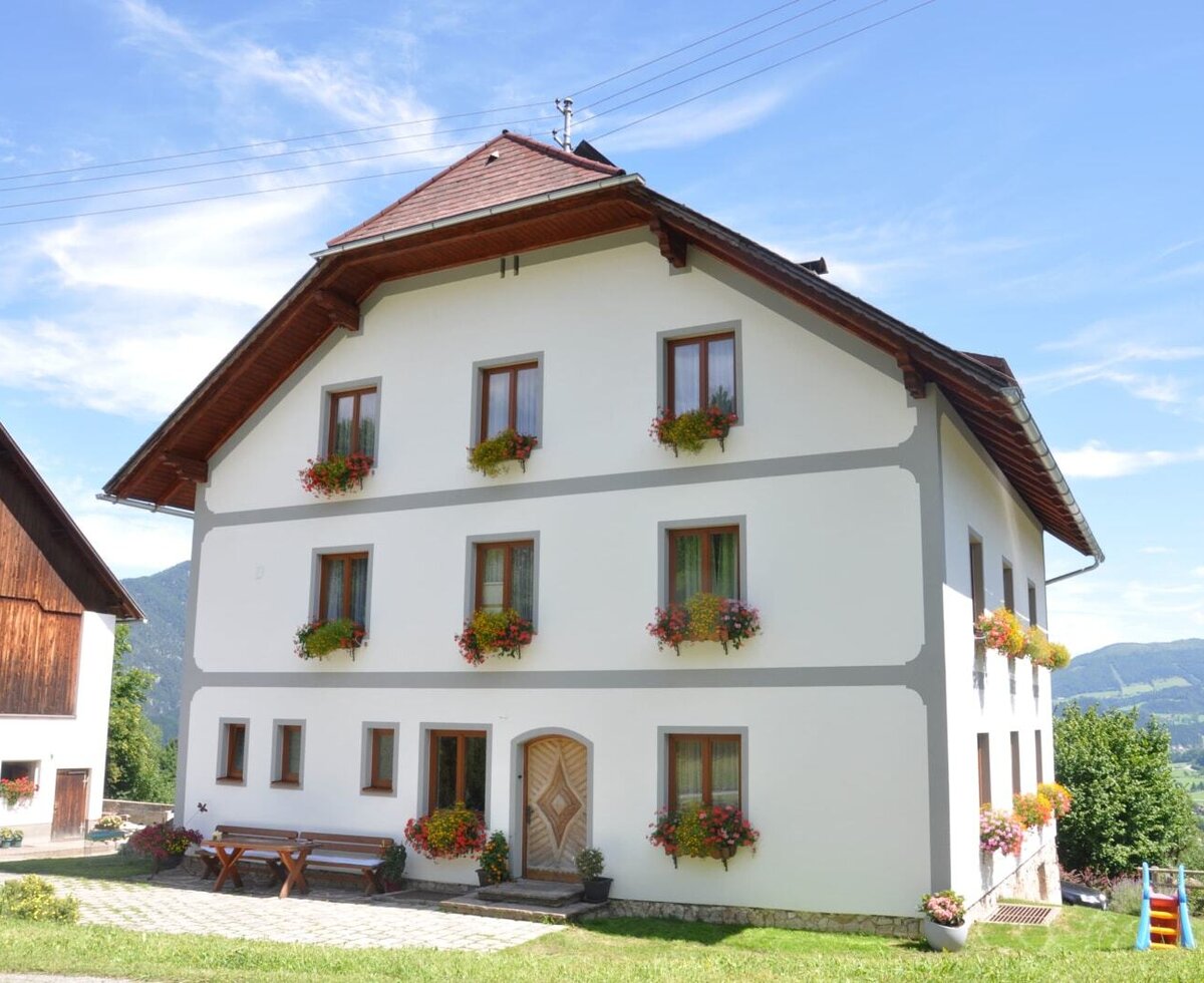 Das Bauernhofgebäude mit blumengeschmückten Fenstern, Sitzbänken im Freien und einer kleinen Rutsche auf der Rasenfläche.