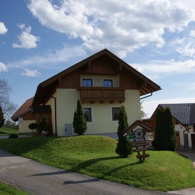 Der Bauernhof von außen mit Balkon und grüner Rasenfläche.