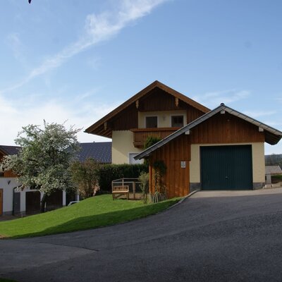 Außenansicht des Bauernhofs mit Garage, Gartenbereich mit Bank und Balkon.