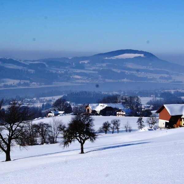 Blick vom Bauernhof auf die verschneite Landschaft mit See und Bergen.