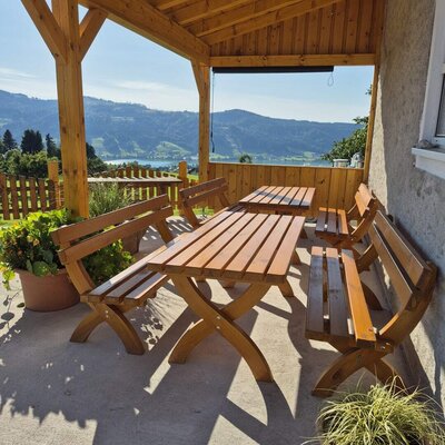 Überdachter Balkon des Bauernhofs mit Holztisch und Bänken und Blick auf den See und die Berge.