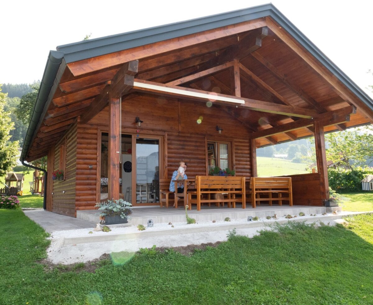 Die Holzhütte auf dem Bauernhof mit überdachter Terrasse, Holztisch und Sitzbänken.