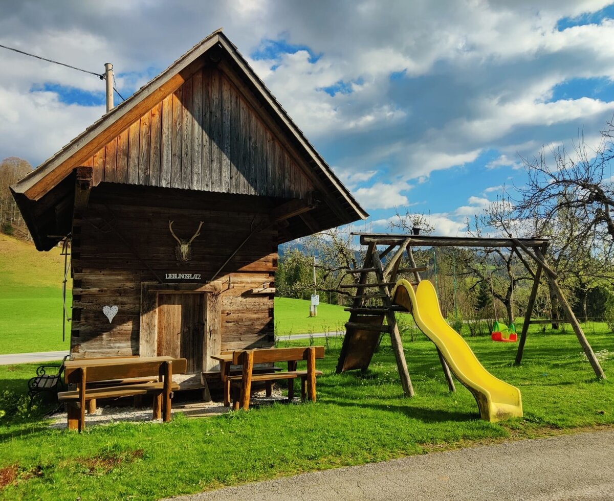 Spielplatz mit Rutsche und Schaukeln sowie eine Holzhütte mit Sitzgelegenheiten auf dem Bauernhof.