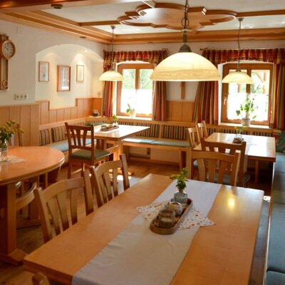 Der Frühstücksraum im Bauernhof mit Holztischen, Bänken, Stühlen und einem traditionellen Kachelofen.
